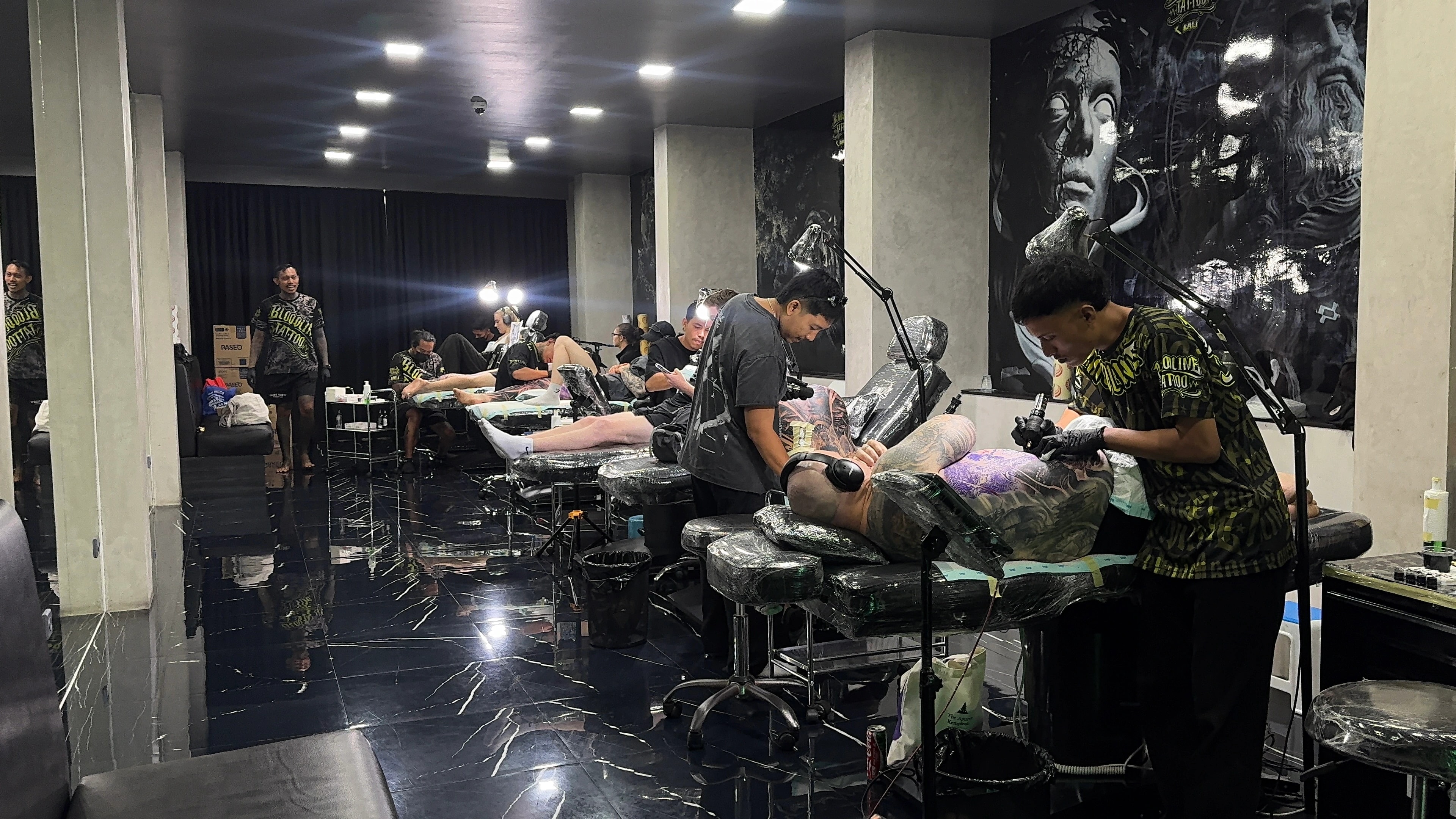 Professional tattoo artists working in the sterile Bloodline Tattoo Bali studio with black and grey realism murals and clinical session standards